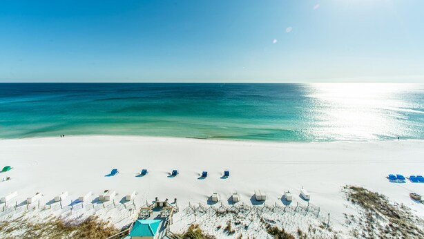 Een strand met wit zand, helder turquoise water en een rij blauwe ligbedden.