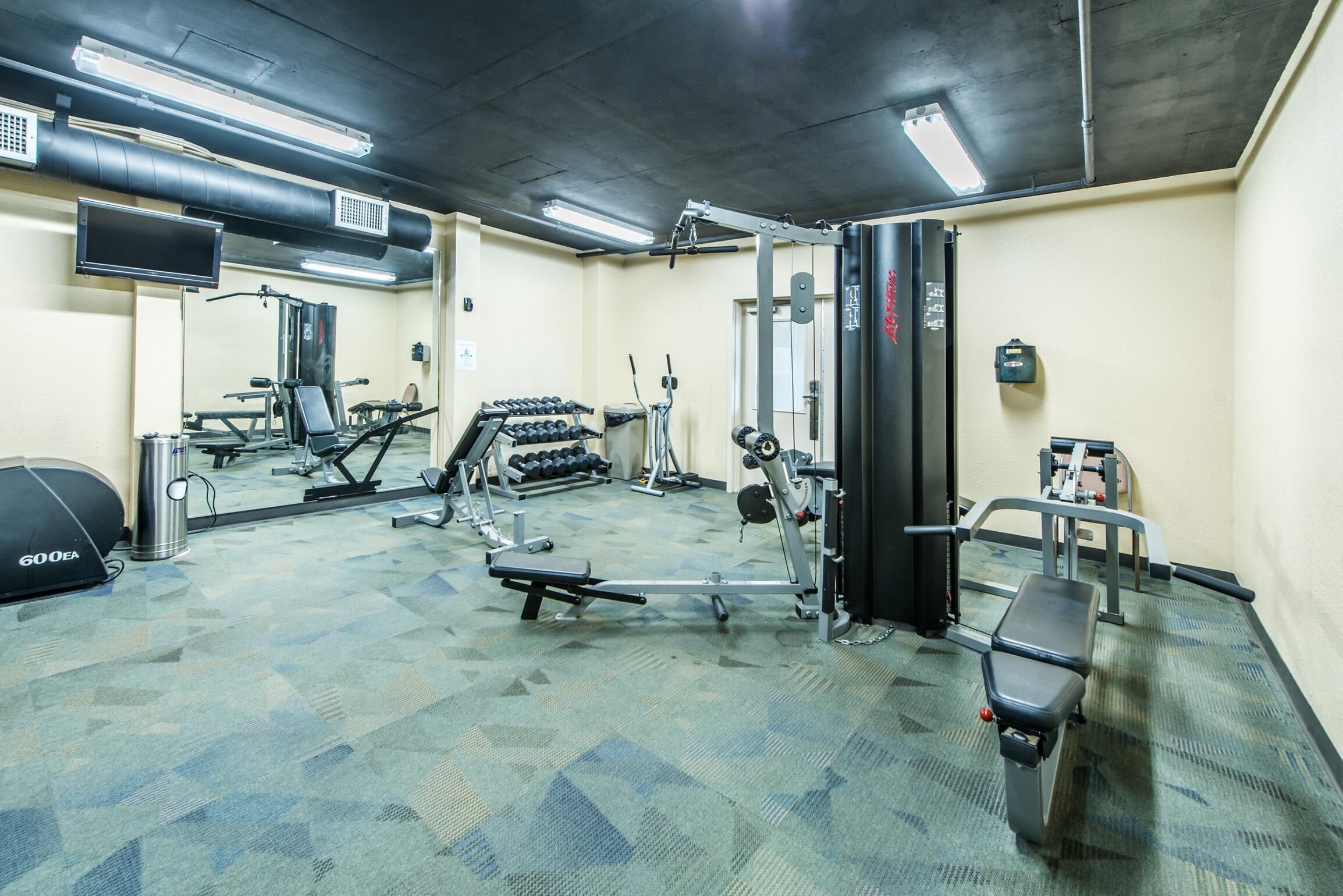 A gym with various exercise equipment, a mirror, and a TV on the wall.