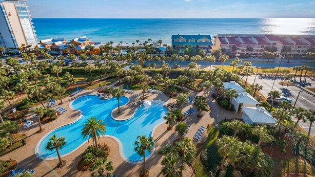 A resort with a large pool, palm trees, and a view of the ocean. - Sterling Shores 916 (Destin)