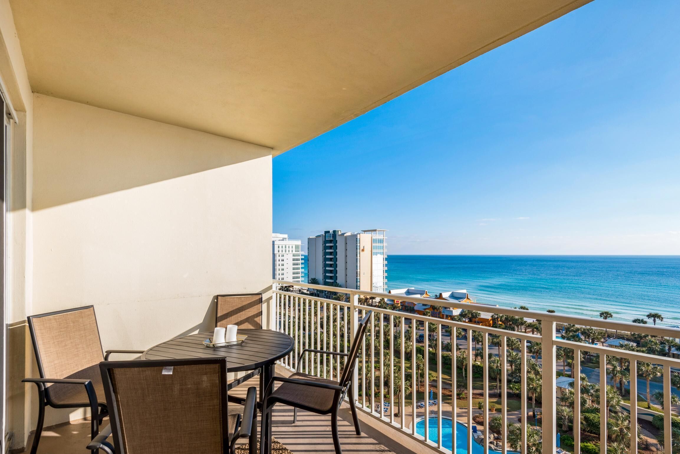 A balcony with a table and chairs, overlooking a beach and ocean with buildings in the background.