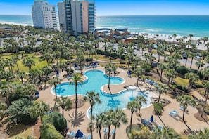 Um resort com uma piscina grande, palmeiras e vista para o oceano.