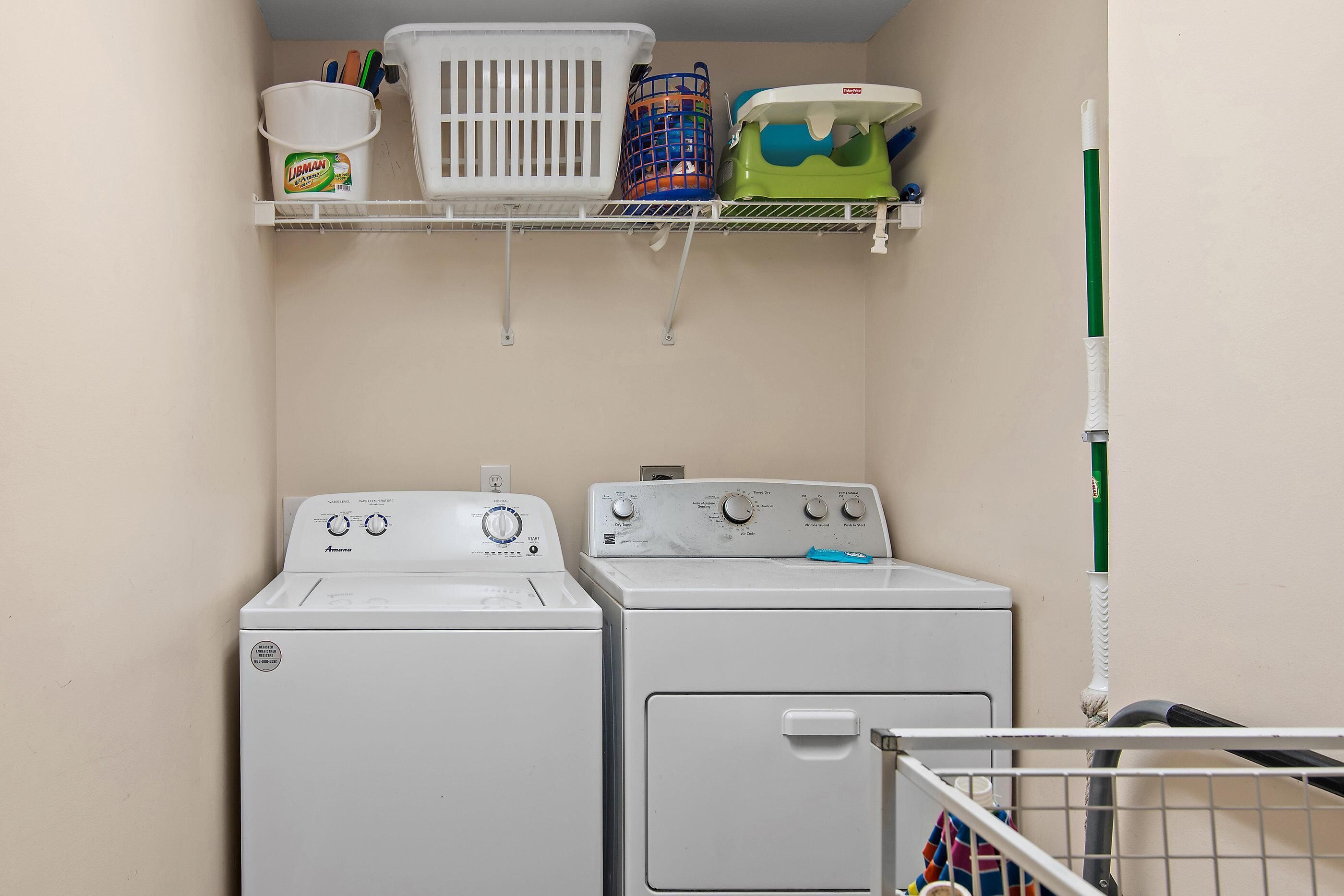 A laundry area with two washing machines, a shelf with laundry baskets, and a mop.