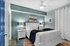 A bedroom with a white bed, teal walls, a ceiling fan, and a nightstand with a lamp. - Sterling Shores 215 (Destin)