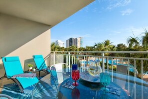 A balcony with turquoise chairs, a glass table, and a view of a swimming pool and buildings. - Sterling Shores 215 (Destin)