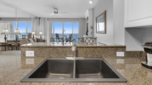 A modern kitchen with granite countertops, a double sink, and a view of the ocean. - Sterling Sands 707 (Destin)