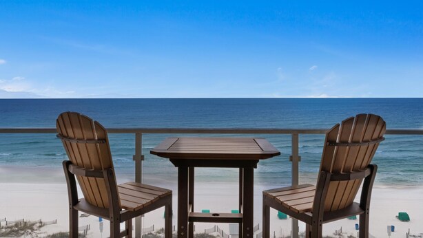 A wooden table and two chairs on a balcony overlooking a beach with a clear view of the ocean. - Sterling Sands 707 (Destin)