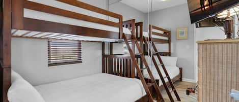 A room with bunk beds, a ladder, a small table, and a television on the wall.
