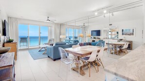 A modern living room with a large dining table, blue sofas, and a view of the ocean. - Sterling Sands 502 (Destin)
