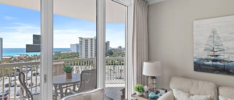 A balcony with a view of the city and ocean, furnished with a sofa, chair, and table.
