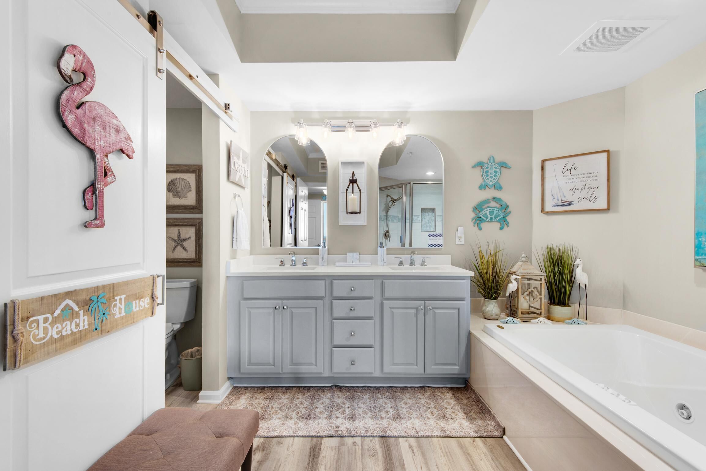 A bathroom with a double vanity, a large bathtub, and a wooden sign that reads "Beach House".