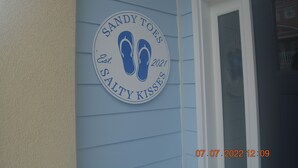 Un panneau circulaire sur lequel on peut lire « Sandy Toes Salty Kisses » et qui représente une paire de tongs.