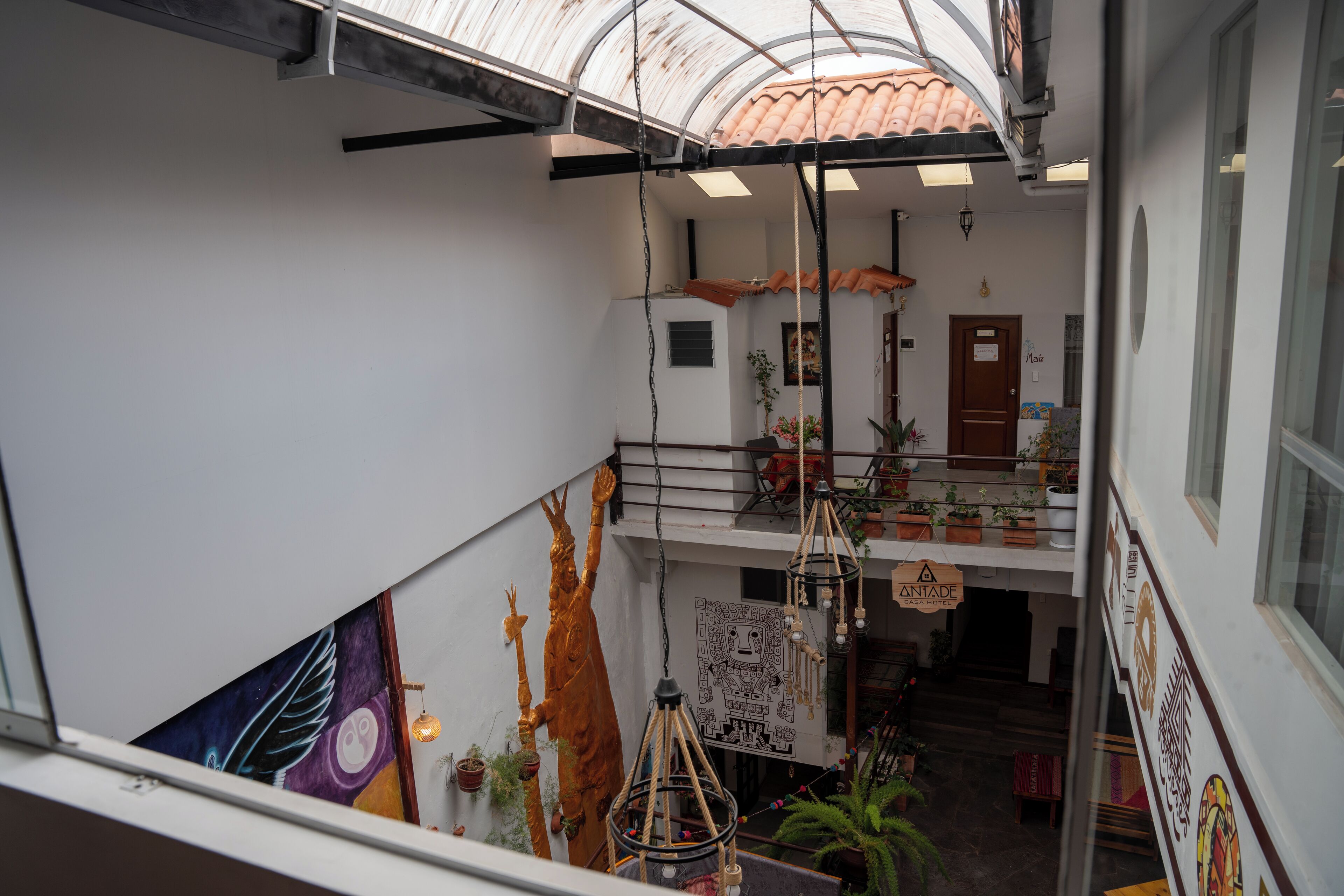 Ein mehrstöckiges Interieur mit Balkon, hängenden Pflanzen und Wandgemälde.