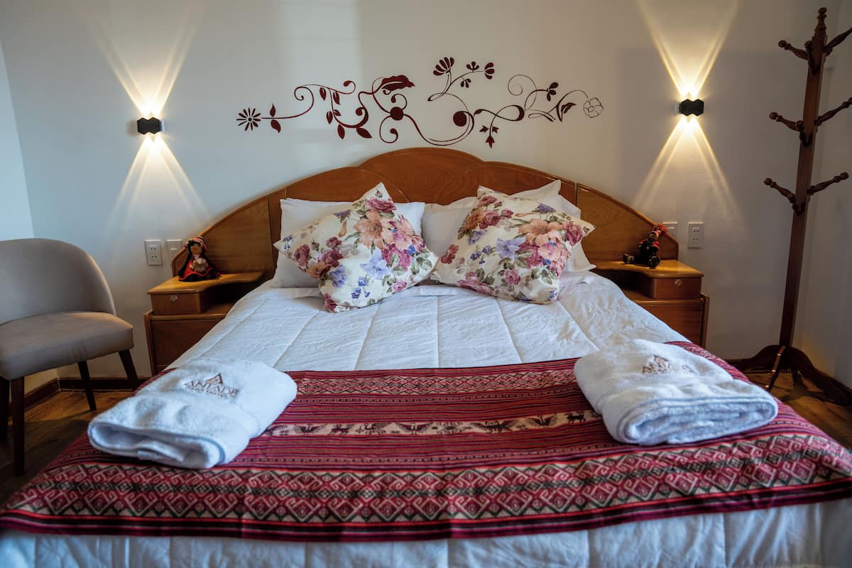 Una cama bien hecha con almohadas estampadas con flores, una colcha roja con diseño y dos toallas blancas.
