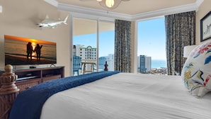 A hotel room with a large bed, a television mounted on the wall, and a view of the city and ocean through large windows. - St. Lucia 1103 (Destin)