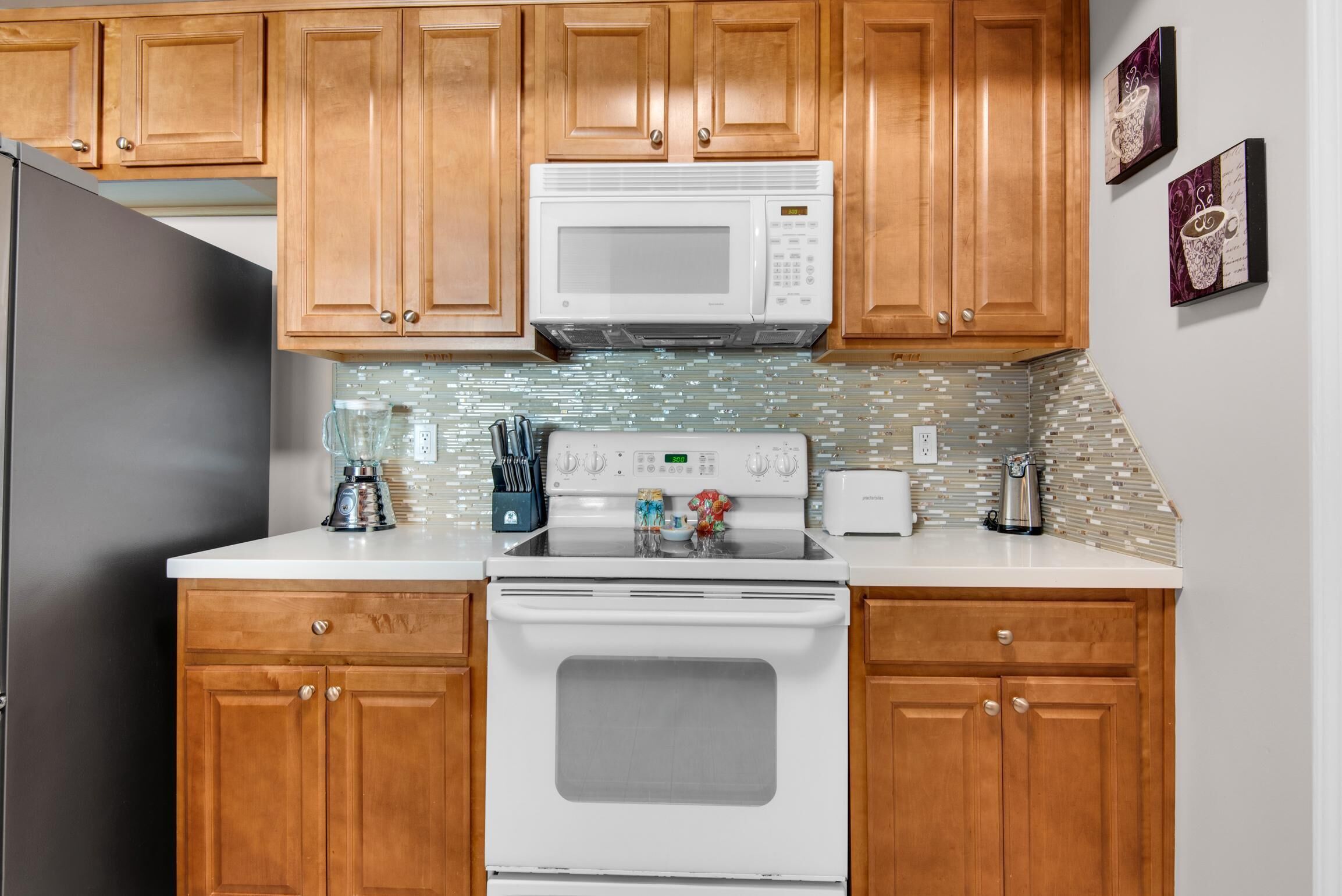 A kitchen with wooden cabinets, a white microwave, a stove, and a blender on the counter.