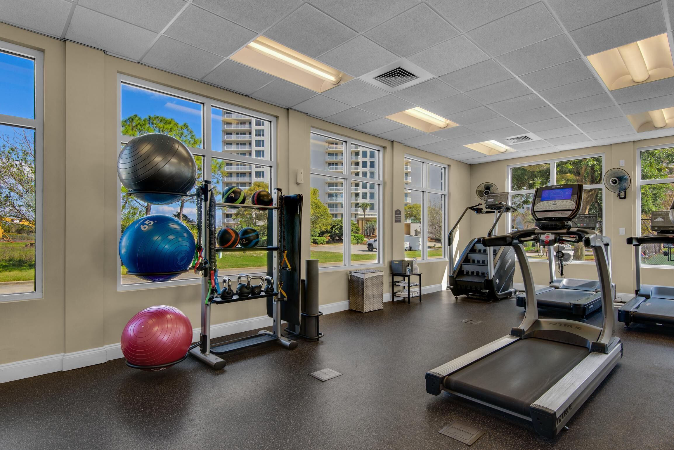 Ein Fitnessstudio mit Trainingsgeräten, großen Fenstern und Laufband.