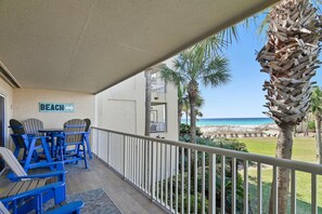 A balcony with a view of the beach, blue Adirondack chairs, and a sign that reads 'BEACH'.