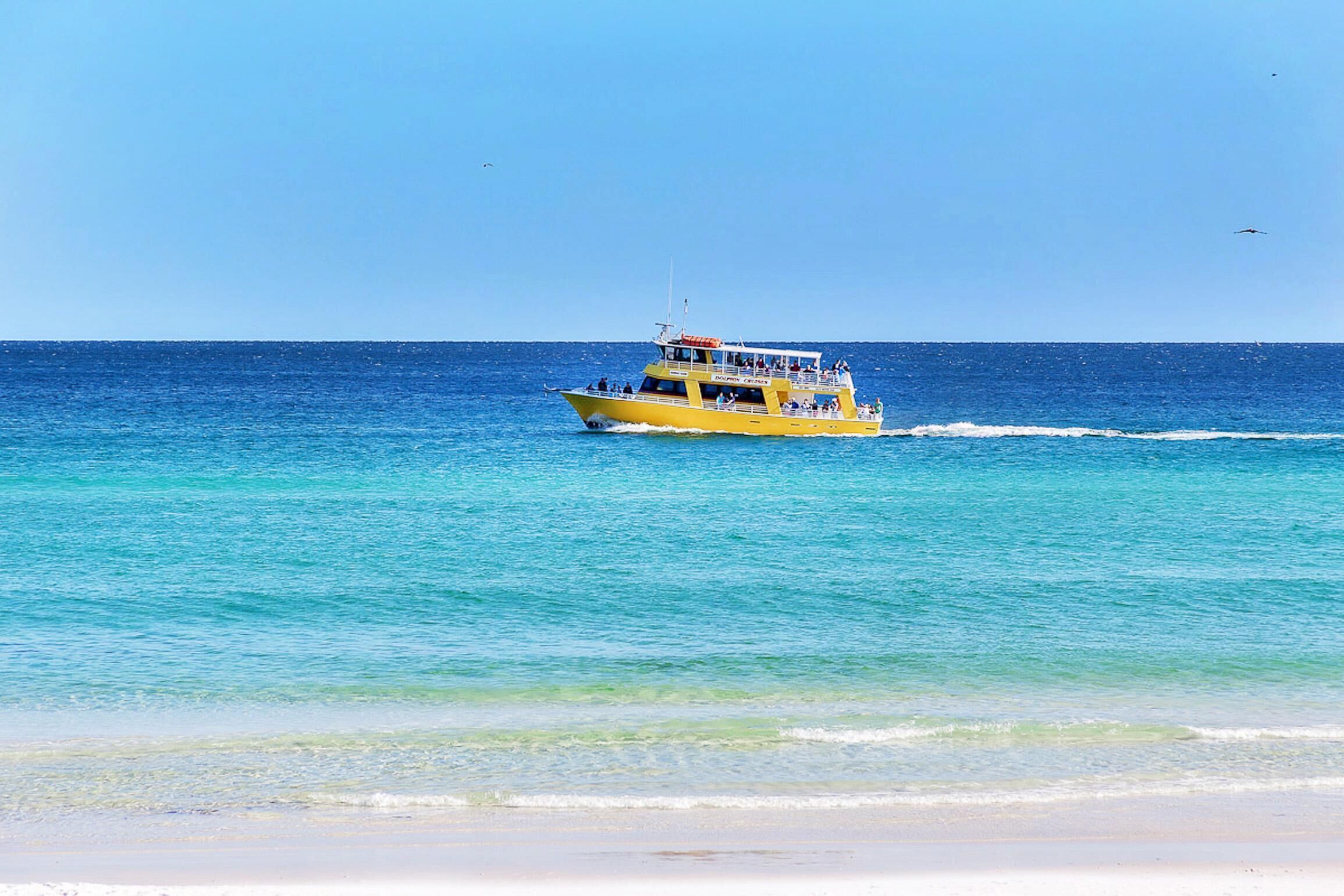 A yellow boat on a clear blue sea with a sandy beach in the foreground.