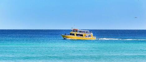 A yellow boat on a clear blue sea with a sandy beach in the foreground.