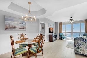 A spacious living room with a dining area, a TV, and a balcony with a view.