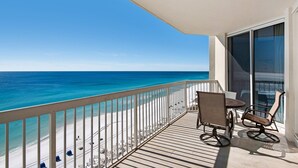 Een balkon met uitzicht op de oceaan, een tafel met stoelen en een grote schuifdeur van glas.