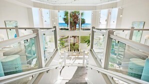 Een modern hotelinterieur met een trap die leidt naar een balkon met uitzicht op het strand.