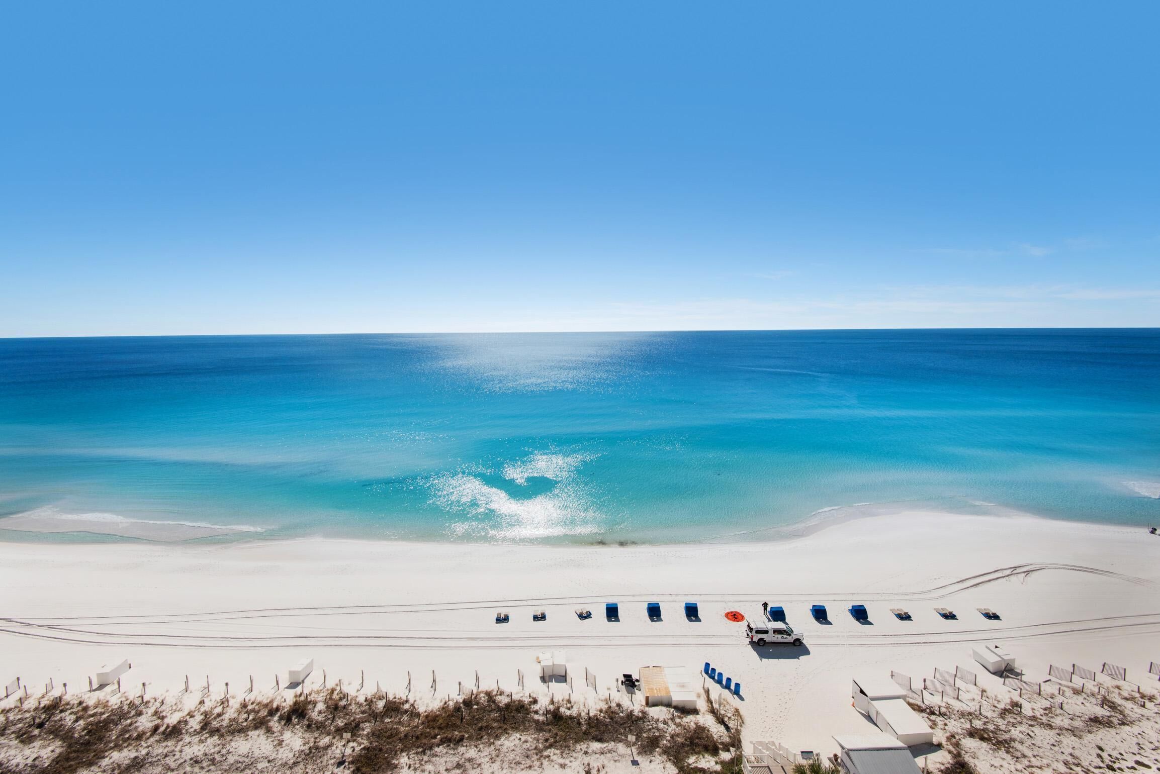 Ein Strand mit weißem Sand, klarem, blauem Wasser und einer Reihe blauer Liegestühle.