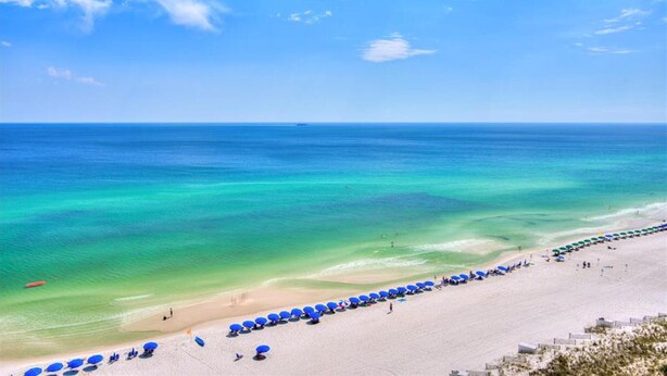 Een strand met helder turquoise water, een zandstrand en rijen blauwe parasols.
