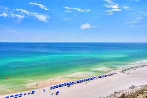 A beach with clear turquoise waters, a sandy shore, and rows of blue umbrellas.