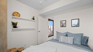 A bedroom with a bed, pillows, a white wall, a door, and a window.