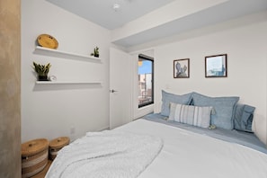 Une chambre à coucher avec un lit, des oreillers, un mur blanc, une porte et une fenêtre.