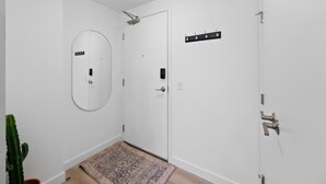 A hallway with white walls, a door with a mirror, a coat rack, and a potted plant.