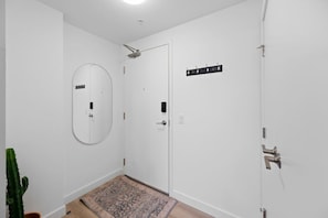 Un couloir aux murs blancs, une porte avec un miroir, un porte-manteau et une plante en pot.