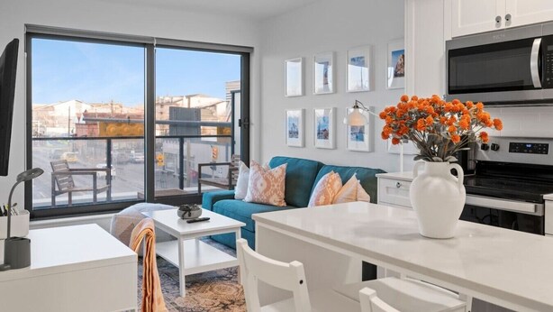 A modern apartment with a dining area, a sofa, a kitchen with a microwave, and a view through large windows.