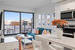 A modern apartment with a dining area, a sofa, a kitchen with a microwave, and a view through large windows.
