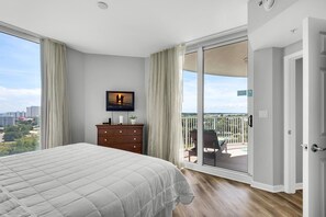 Une chambre dotée d’un grand lit, d’un téléviseur fixé au mur, d’une commode et d’une porte-fenêtre coulissante donnant sur un balcon avec vue sur la ville.