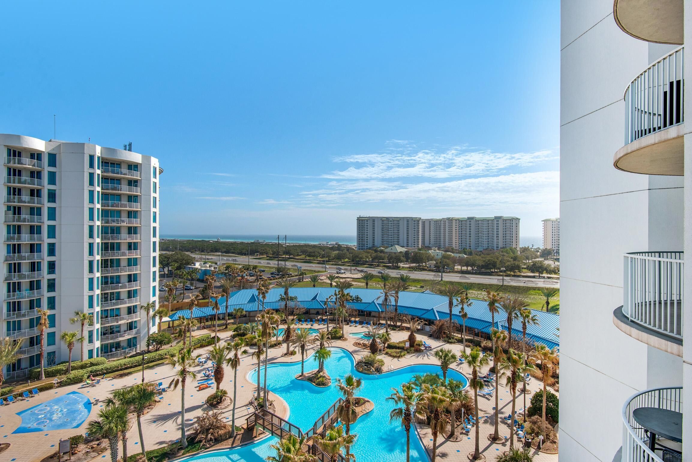 Een resort met een groot zwembad, palmbomen en hoge gebouwen op de achtergrond.