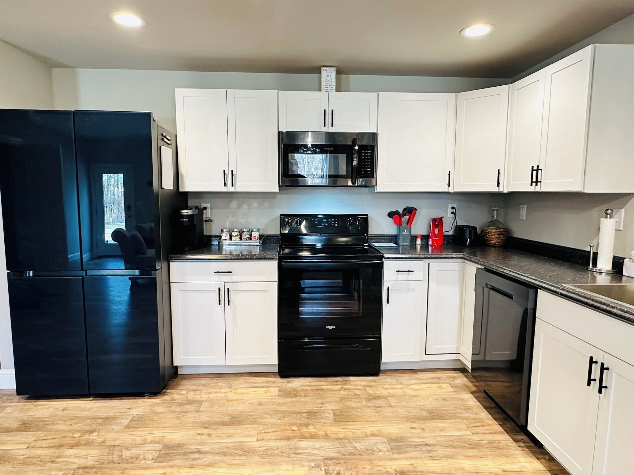 A modern kitchen with white cabinets, a black refrigerator, a microwave, and a stove.