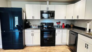 A modern kitchen with white cabinets, a black refrigerator, a microwave, and a stove.