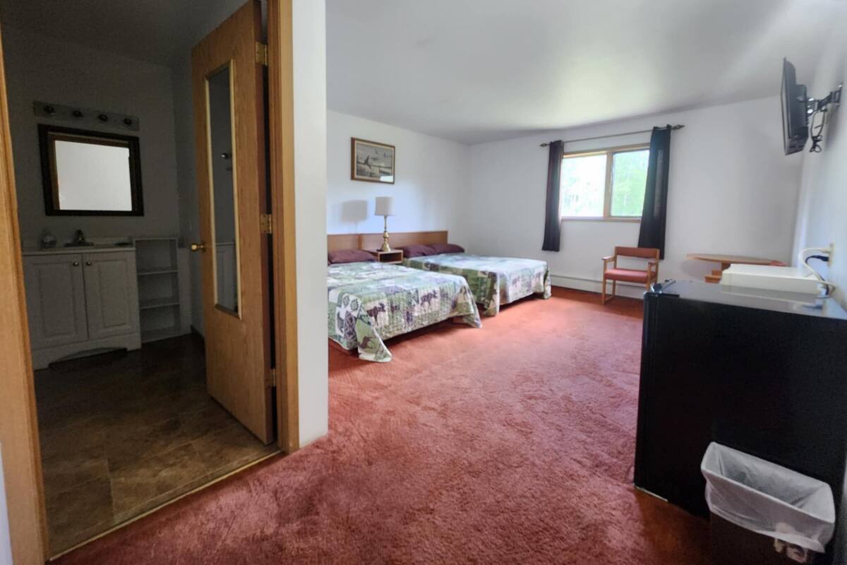 A room with two beds, a desk, a mirror, and a window.