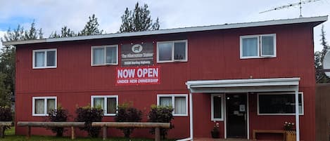 A red building with a sign indicating it is now open under new ownership.