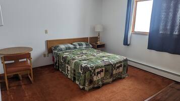 Quarto com cama, cadeira, mesa de cabeceira, luminária e janela com cortinas.