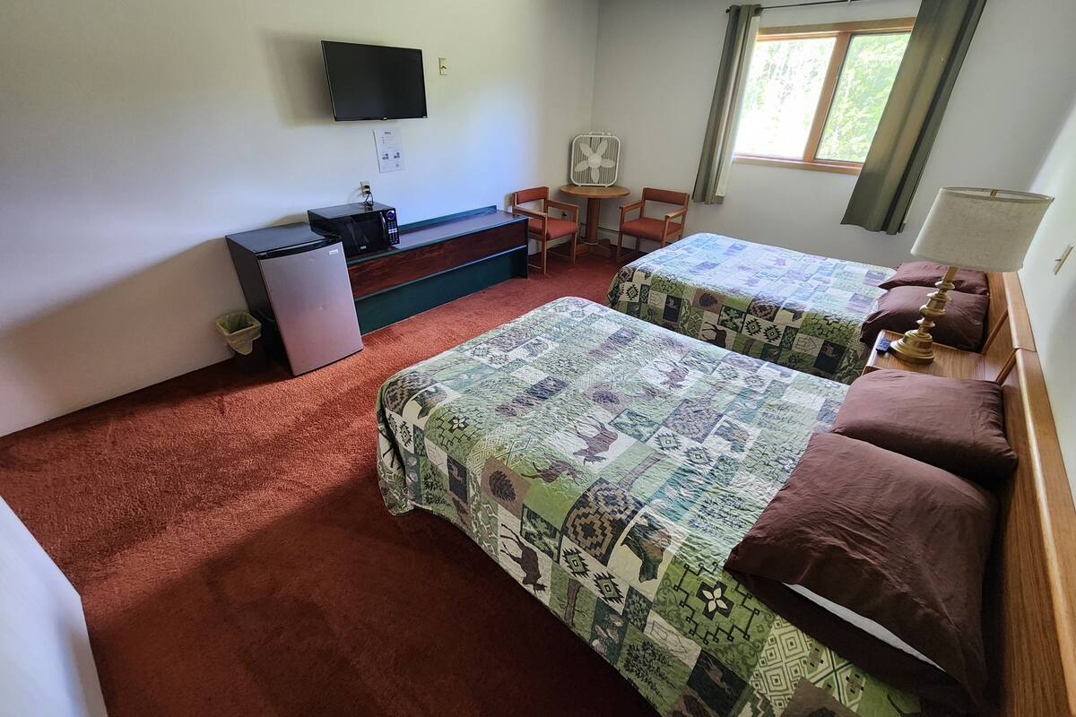 A room with two beds, a desk, a chair, a TV, and a window with curtains.