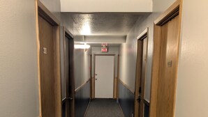 A hallway with carpeted floors, wooden doors, and a fire alarm on the wall. - The Hibernation Station (Sterling)
