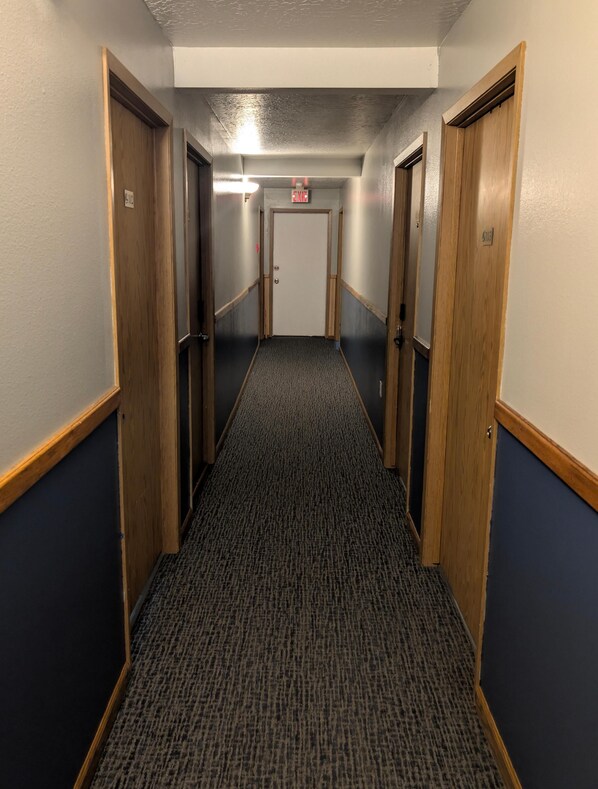 A hallway with carpeted floors, wooden doors, and a fire alarm on the wall.