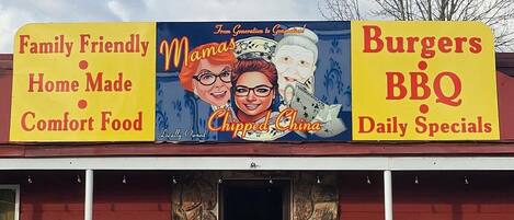 Restaurante com um letreiro anunciando 'Comida Caseira e Confortável para a Família' e 'Hambúrgueres, Churrasco e Pratos Especiais Diários'.