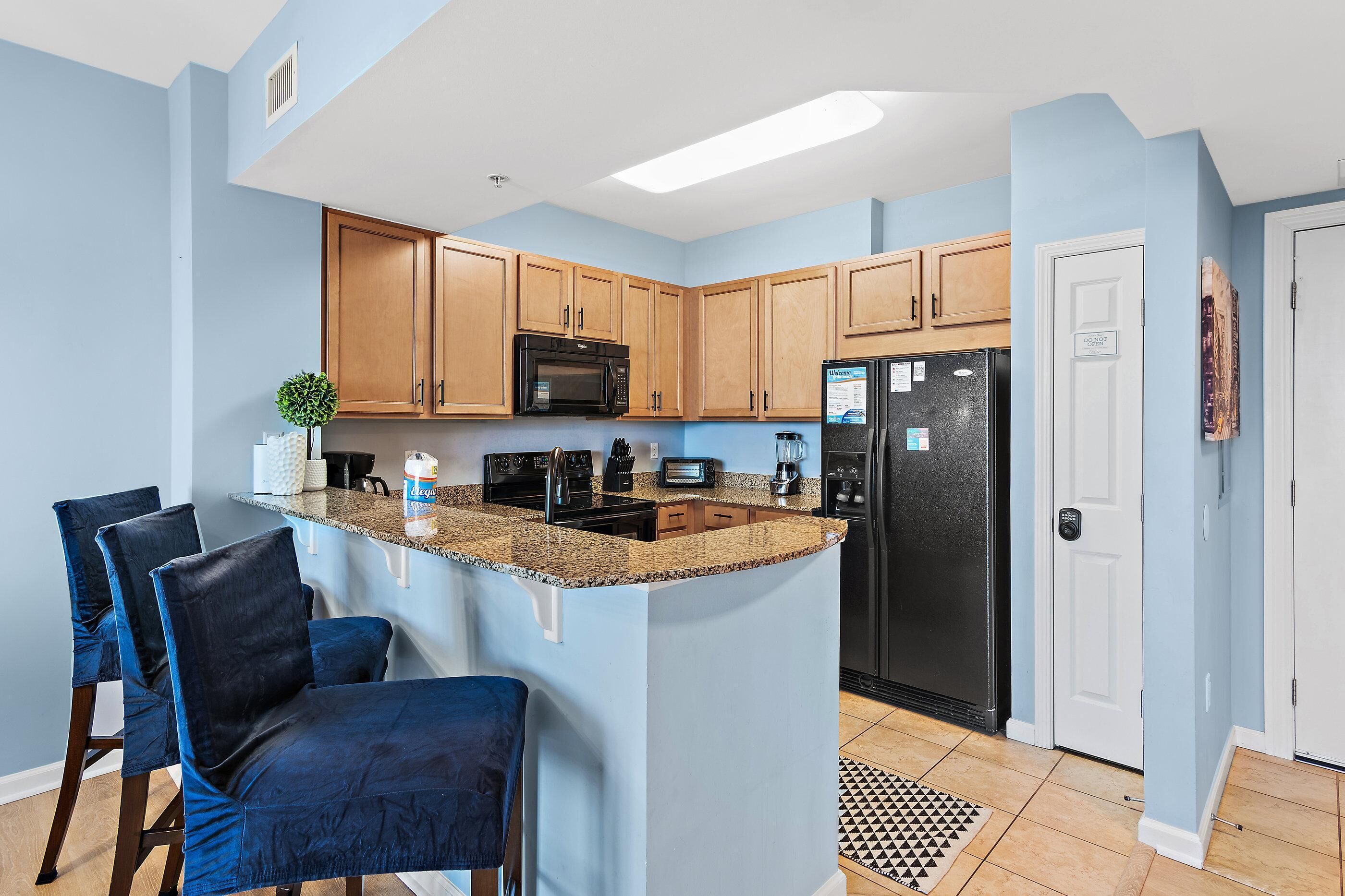 A kitchen with blue walls, wooden cabinets, a black refrigerator, and a granite countertop.