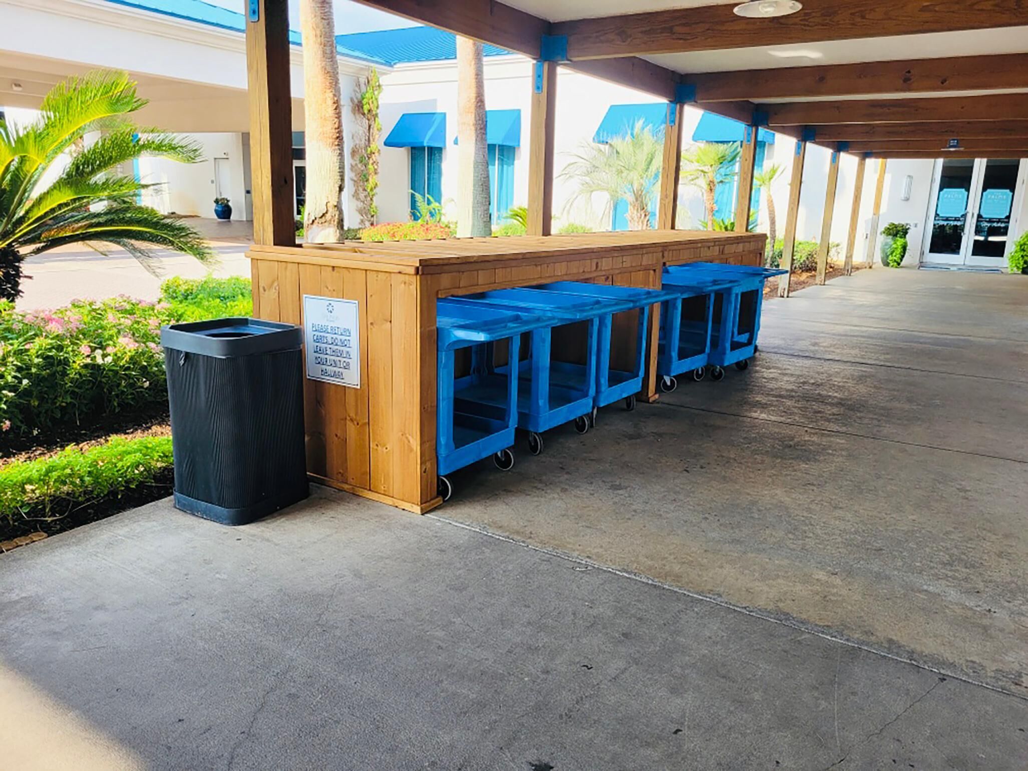A covered outdoor area with a wooden counter, blue trash bins, and a black trash can.