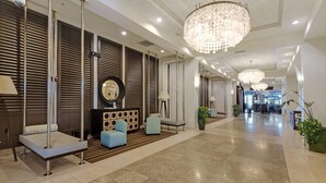 A modern hotel lobby with a reception desk, seating area, and a chandelier.