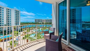 A balcony with wicker chairs and a view of a resort with multiple pools and buildings in the background.